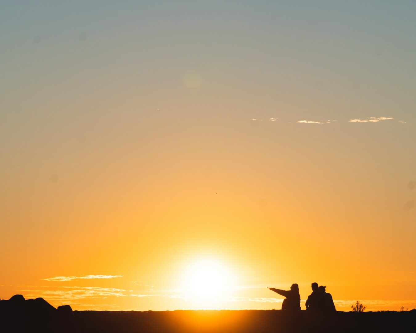 silhouette of three people sitting on land during golden hour