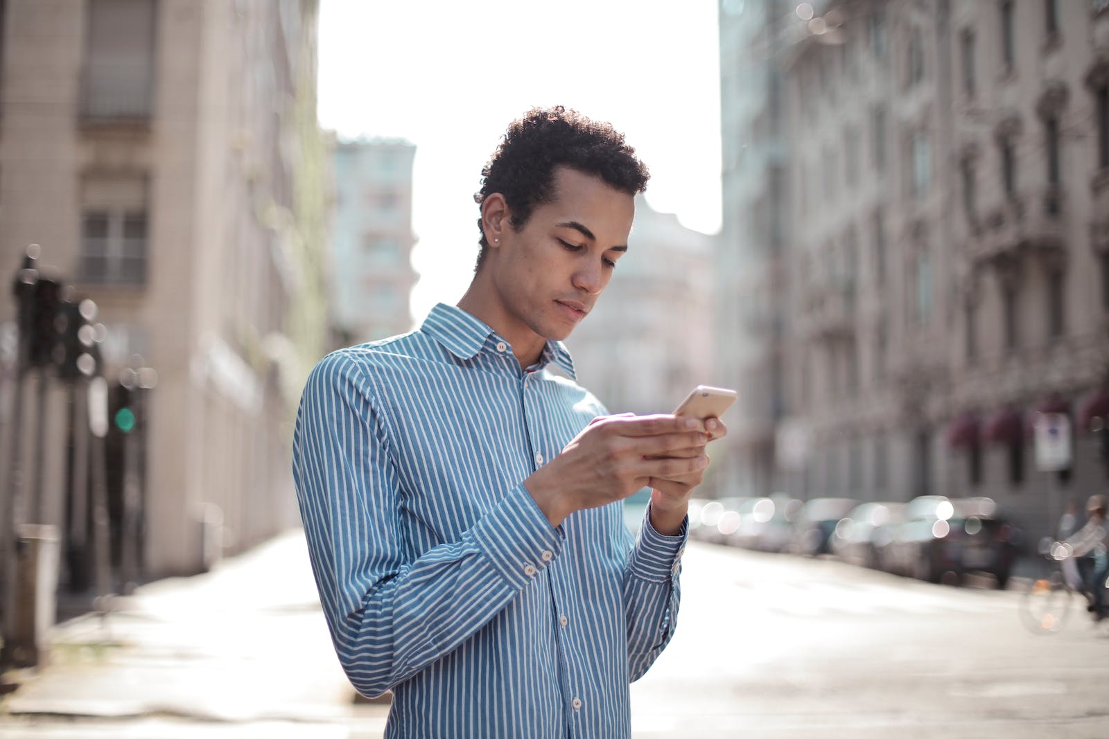 Concentrated ethnic guy surfing smartphone on street
